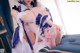 A woman in a maid outfit is sitting on a bed.